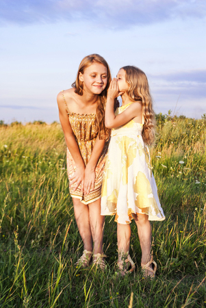 Two girls standing in a field , smiling and sharing a secretの写真素材
