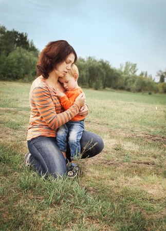 Mom and his little son are hugging on the background of a green glade.の写真素材