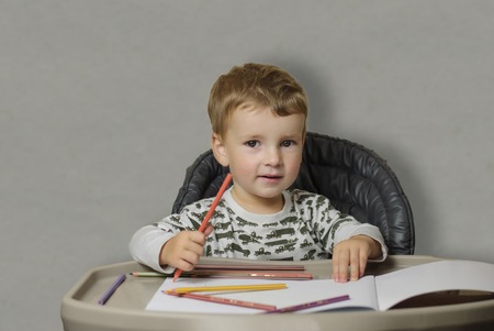 little boy draws with colored pencils, sits at the tableの写真素材