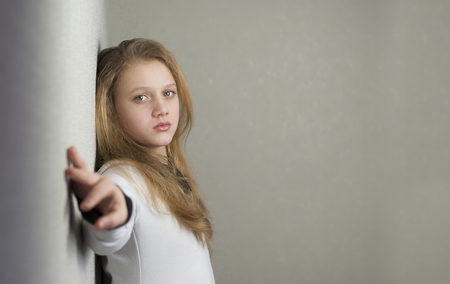 Portrait of sad blond teen girl standing near wallの写真素材