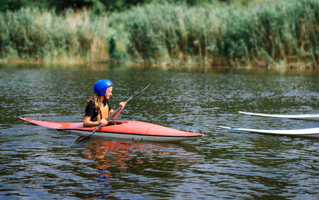 young teenager girl actively manages a sports kayak boat on a beautiful riverの写真素材