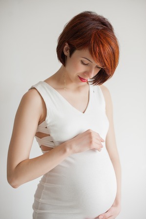 Happy young pregnant woman in white dress touching her bellyの写真素材