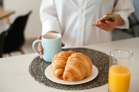 Woman in white shirt drinking morning coffee with croissantsの写真素材