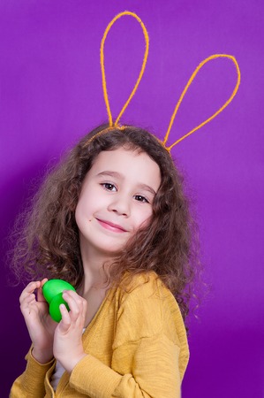 Cheerful little child girl with bunny ears with two Easter eggs on a colored background. Happy...