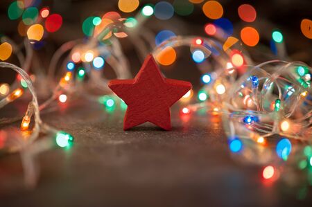 Wooden toy in the shape of a red star on a background of Christmas lights. New Year's and Christmas. Selective focusの写真素材