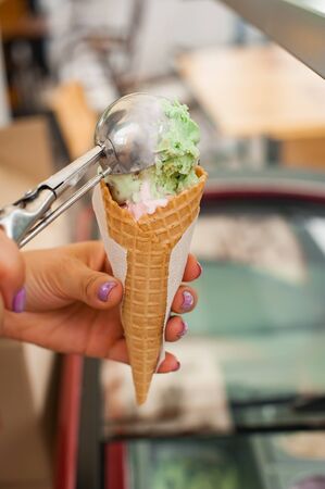 Pistachio and vanilla ice cream cone on wooden background. Girl puts a ball of ice cream in a waffle...