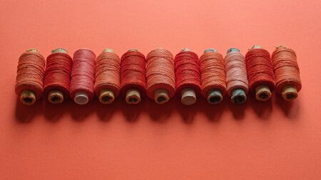 A coral spool of threads on coral paper background, with copy space. Coral color