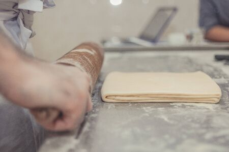 The process of preparing puff pastry in a bakery. The baker rolls the dough. Selective focusの写真素材