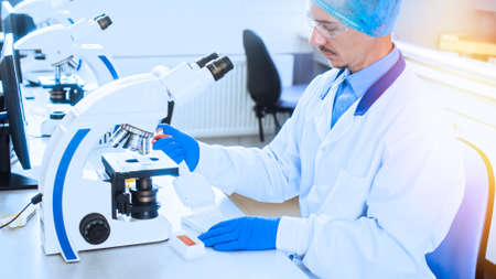 A laboratory worker examines viruses through a microscopeの写真素材
