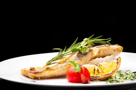 Fried fish with rice on a white plate. Black wooden background.