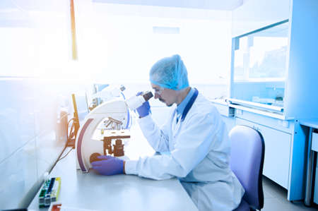 A laboratory worker examines viruses through a microscope