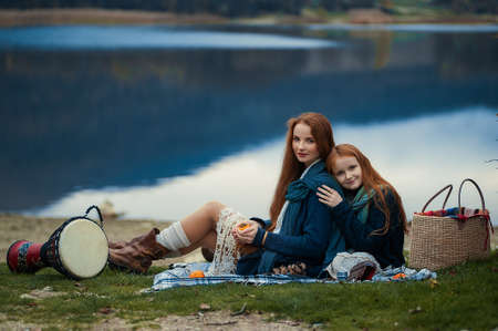 A young woman and a girl with red long hair sitting on a blanket in autumn. Boho styleの写真素材