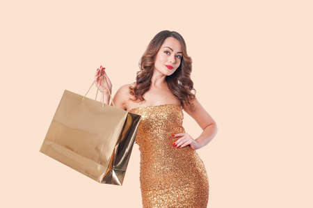 Woman in fashion clothing with a gold paper bag on a beige backgroundの写真素材