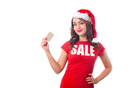 Woman in Santa hat and a red t-shirt with the inscription sale holds a card over white backgroundの写真素材