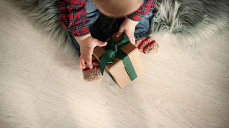 Baby boy in a plaid shirt sitting near a garland holding a box with a giftの写真素材
