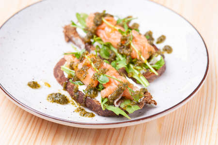 Salmon bruschettes with cheese cream, microgreen and sauce on plate. Horizontal shot.