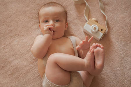 Baby with a wooden camera lies on a beige background The baby sucks his thumbの写真素材