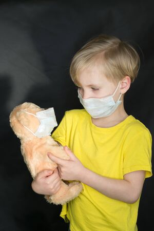 Child in a medical mask with a toy bear in his arms on a black background. The game of the doctor. The concept of protection against viruses and diseases. Stop coronovirus. Covid-19.の写真素材