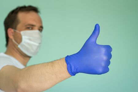 Portrait of attractive man in a medical mask and a glove on a blue background. Pandemic Protection Concept. No to coronovirus. Covid-19.の写真素材