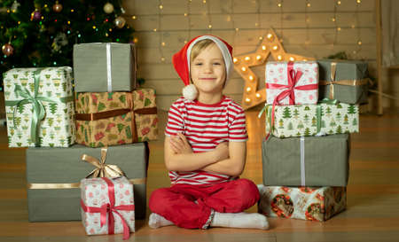 Smiling child in a red Santa Claus hat with a Christmas present on the background of a Christmas tree. New Years magic. Christmas conceptの写真素材