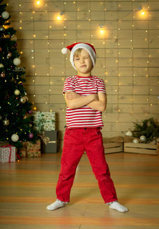 Smiling child in a red Santa Claus hat with a Christmas present on the background of a Christmas tree. New Years magic. Christmas conceptの写真素材