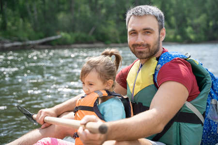 A father and daughter in life jackets are rafting down a mountain river. Summer family adventures. Rafting on a mountain river on a raft.の写真素材