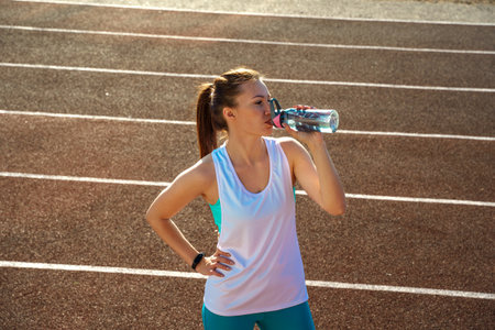 Attractive girl drinking water after doing sports on the treadmill at the stadiumの写真素材