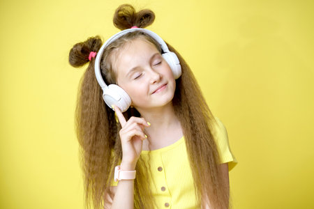 Cool pretty girl with trendy hairstyle in headphones listens to music on yellow backgroundの写真素材