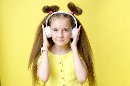 Cool pretty girl with trendy hairstyle in headphones listens to music on yellow backgroundの写真素材