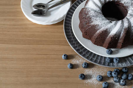 Homemade vegan chocolate cake, sprinkled with powdered sugar. Blueberries and dessert dishes. Top view with copy space. Selective focus.の写真素材
