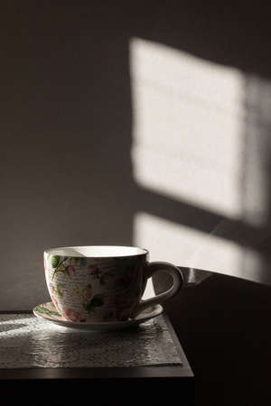 A mug with a floral pattern on the table, beautiful shadows and highlights. Vertical photo.の写真素材