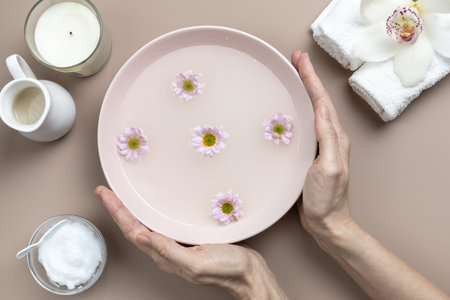 Female hands holding bowl of water and flowers. Home skin care, hands spa, relaxation.の写真素材