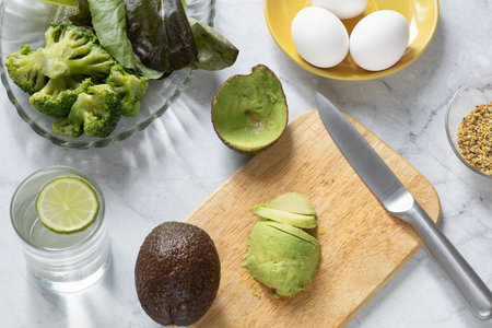 Cooking breakfast with eggs, avocado, broccoli, greens and infused lime water. Metabolism boosting food. Top view.の写真素材