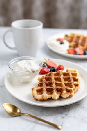 Vertical photo of sweet breakfast. Croffles (croissant waffle) with whipped cream and berries, cup of coffee.の写真素材