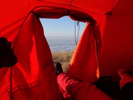 view from the bright red tent on the valley to the exit of the tent stretched legs in red trousers and Hiking bootsの写真素材