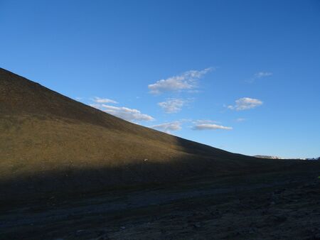 the first rays of the sun illuminate the mountain slope of the pass against a background of bright blue sky and white cloudsの写真素材