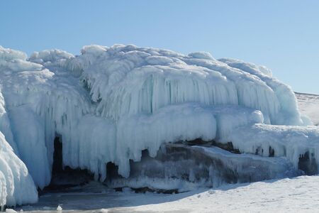 blue ice from frozen waves on a large boulder against a blue sky
