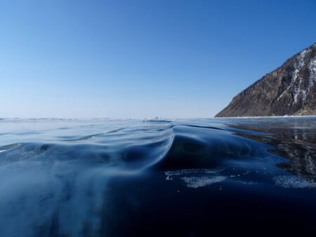 The icy dark blue surface with frozen waves of lake Baikal is visible to the horizonの写真素材