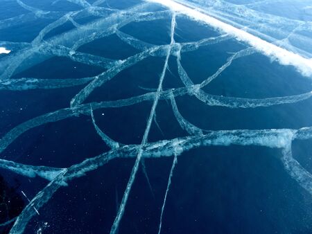 a pattern of white cracks on dark blue transparent ice close- up