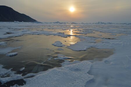 The rays of the setting sun reflect off the icy surface of the lakeの写真素材