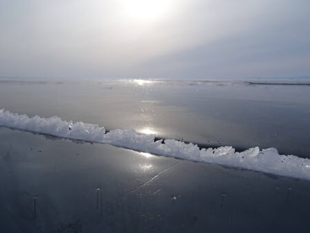 early morning, gray sky and white ice crystals grow from an ice crack on the surface of a frozen lakeの写真素材