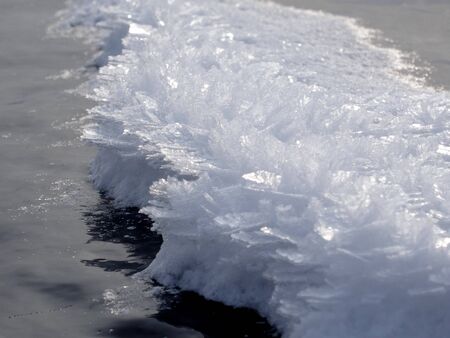 a band of white sparkling snow crystals on the dark smooth ice of the lakeの写真素材