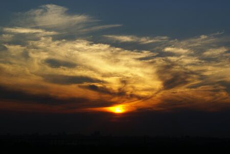 the bright circle of the sun inside the bright colored clouds of the evening sunsetの写真素材