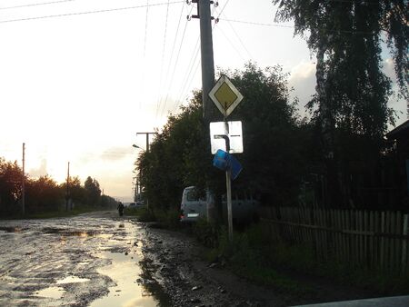 The evening sun is reflected in the puddles on the village street after the rainの写真素材