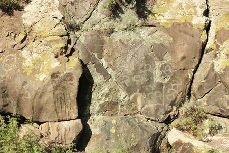 On a vertical rock wall ancient and modern drawings framed by greeneryの写真素材