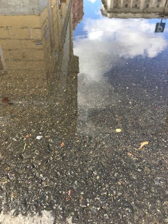 the water of the puddle reflects the sky and stone buildingsの写真素材