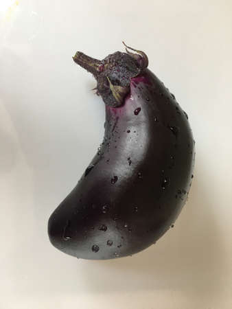 on a white table is a bright purple eggplant. there are drops of water on itの写真素材