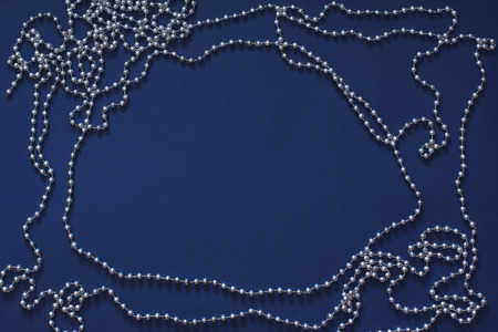 Frame of silver beads for a Christmas tree on a dark blue background. New year decorations. Top view, flat layの写真素材