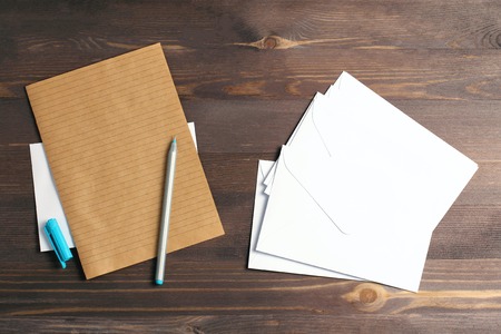 Stack of white envelopes on a wooden background. A blue handle and a sheet of kraft paper. Flat lay, top viewの写真素材