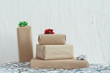Stack of gifts in kraft paper with bow of green, red and silver colors. Plaster wall. Copy space,...